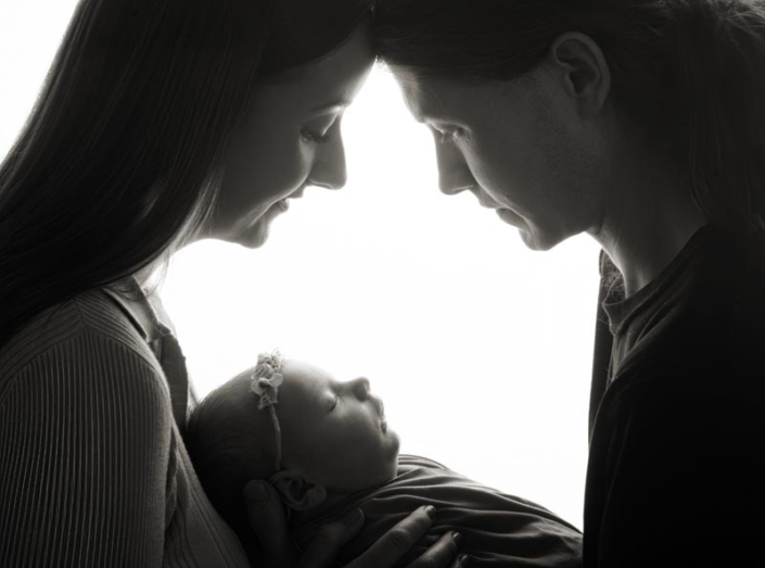 mum dad and newborn baby girl backlit